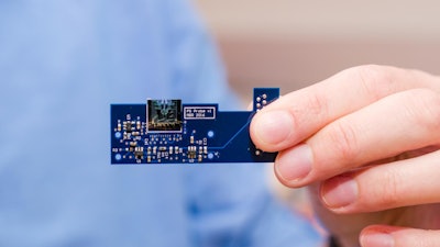 A MEMS-based atomic force microscope developed by engineers at the University of Texas at Dallas is about 1 square centimeter in size (top center). Here it is attached to a small printed circuit board that contains circuitry, sensors and other miniaturized components that control the movement and other aspects of the device.
