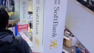 In this Nov. 7, 2016, file photo, a shopper standing on an escalator passes by the company logo of SoftBank at an electronic shop in Tokyo. The $3.3 billion acquisition by SoftBank Group Corp., the Japanese telecommunications, internet and solar energy giant, of Fortress Investment Group marks tycoon Masayoshi Son’s latest step in building a technology investment empire.