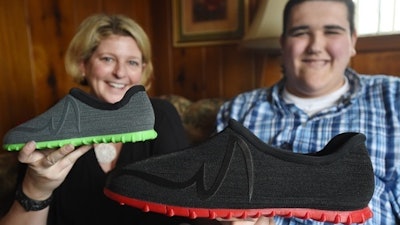 In a Wednesday, March 1, 2017 photo, Broc Brown, right, shows off his new shoes with Feetz CEO Lucy Beard at his grandmother's home in Michigan Center, Mich. Brown, who has Sotos Syndrome and is 7 feet, 8 inches tall, was given a new pair of about size 28 shoes from Feetz. Feetz is a company that uses an app to convert photos of someone’s feet into a 3-D model, which can be measured to create custom-fit shoes manufactured by a 3-D printer.
