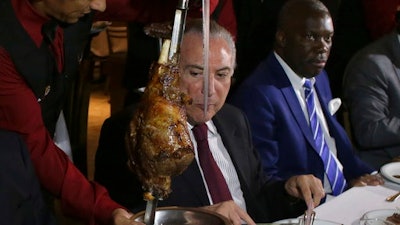 Brazil's President Michel Temer, center, alongside Angola's Ambassador to Brazil, Nelson Manuel Cosme, attend a steak dinner at a traditional Brazilian barbecue restaurant after a meeting on the rotten meat scandal in Brasilia, Brazil, Sunday, March 19, 2017. Temer met with dozens of ambassadors from countries that import Brazilian meat, seeking to minimize damage from a corruption probe that alleges meatpackers bribed inspectors to keep rotten meat on the market.