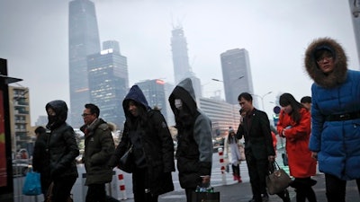 In this Feb. 21, 2017 photo, commuters, some wearing masks, walk to a subway station to a subway station during the evening rush hour in Beijing. Yet the city’s average reading of the tiny particulate matter PM2.5 - considered a good gauge of air pollution - is still seven times what the World Health Organization considers safe. A group of Chinese lawyers is suing the governments of Beijing and its surrounding areas for not doing enough to get rid of the smog.