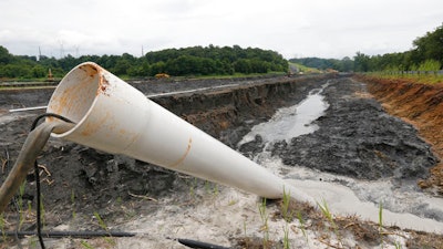 In this Friday June 26, 2015 file photo, a drain pipe sticks out of a coal ash retention pond at the Dominion Power's Possum Point Power Station in Dumfries, Va. The company is moving coal ash from several ponds to one lined pond. As Virginia and its public utilities struggle to cope with the coal ash buried in pits and ponds across the state, tons more of the industrial byproduct is being imported each year.