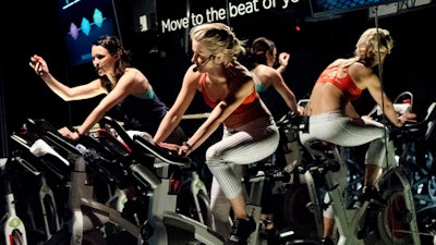 In this March 1, 2017 photo, Jamey Powell, left, and Julianne Hough lead an exercise class as the participants are introduced to the Alta HR fitness tracker at Swerve cycling center in New York. Fitbit is the leading seller of wearable devices, but it’s facing a steep decline because most of its sales are in the U.S., where many people who want a fitness tracker already have one.