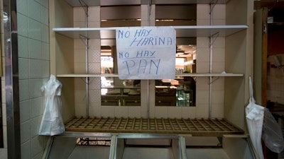 In this March 20, 2017 photo, a sign that reads in Spanish 'No flour. No bread' hangs from an empty shelf at a privately owned bakery in Caracas, Venezuela. The most recent survey on living standards by three major universities found that 93 percent of Venezuelans at the end of last year said they didn't have enough money to buy food, scraping by instead by skipping meals and reducing calories.