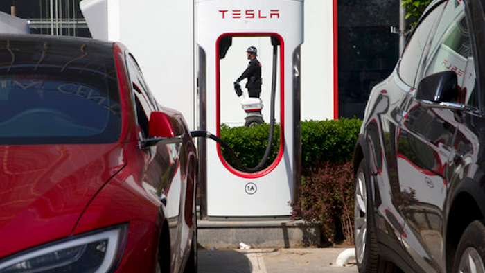 In this Friday, April 14, 2017 photo, a security personnel riding a motorized platform moves past an electric vehicle charging station in Beijing, China. Automakers face a conflict in China's huge but crowded market: Regulators are pushing them to sell electric cars, but buyers want gasoline-hungry SUVs.