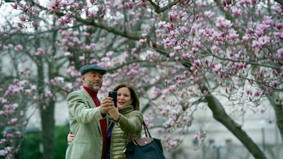 In this Tuesday, Feb. 28, 2017, file photo, Fidelio Desbradel and his wife, Leonor Desbradel, of the Dominican Republic, take a selfie in front of a Tulip Magnolia tree in Washington. A selfie reveals more than whether it’s a good hair day. A company has developed facial analytics technology to help estimate life expectancy by analyzing your face from a photo you upload online. Life insurance companies are interested in the product because it may help them reduce your wait for coverage and boost their sales.