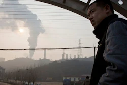 In this Dec. 30, 2016 file photo, a man looks up near smoke spewing from a chimney near the Jiujiang steel and rolling mills in Qianan in northern China's Hebei province. Researchers say Tuesday, April 25, 2017 that China's conversion of coal into natural gas could prevent tens of thousands of premature deaths annually. But there's a catch: It also could undermine efforts to rein in greenhouse gas emissions.