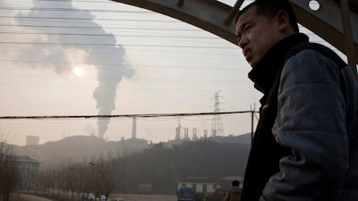 In this Dec. 30, 2016 file photo, a man looks up near smoke spewing from a chimney near the Jiujiang steel and rolling mills in Qianan in northern China's Hebei province. Researchers say Tuesday, April 25, 2017 that China's conversion of coal into natural gas could prevent tens of thousands of premature deaths annually. But there's a catch: It also could undermine efforts to rein in greenhouse gas emissions.