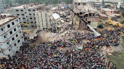 In this April 25, 2013, file photo, Bangladeshi people gather as rescuers look for survivors and victims at the site of a building that collapsed a day earlier, in Savar, near Dhaka, Bangladesh. An international rights group says dozens of global clothing companies are not complying with a plan to ensure better safety in Bangladesh garment factories following the deadly collapse of a building four years ago.