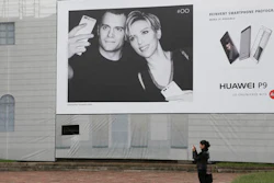 In this Thursday, May 12, 2016 photo, a woman takes a photo in front of Huawei's advertising for the P9 featuring Hollywood stars Henry Cavill and Scarlett Johansson at the Arch of Peace in Milan, Italy. Chinese tech giant Huawei wants Americans to start thinking of it as a stylish smartphone brand. Huawei Technologies Ltd., which pulled out of the U.S. market for network switching gear four years ago due to security fears, became the No. 3 global smartphone seller last year and passed Apple as China’s most popular handset. This year, its 6-year-old consumer brand launched a new flagship, the P9, and is positioning it to compete with Apple and Samsung.