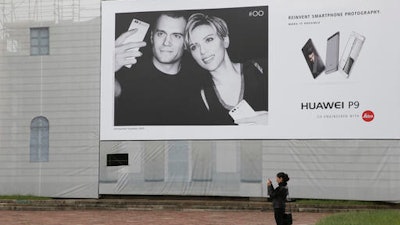 In this Thursday, May 12, 2016 photo, a woman takes a photo in front of Huawei's advertising for the P9 featuring Hollywood stars Henry Cavill and Scarlett Johansson at the Arch of Peace in Milan, Italy. Chinese tech giant Huawei wants Americans to start thinking of it as a stylish smartphone brand. Huawei Technologies Ltd., which pulled out of the U.S. market for network switching gear four years ago due to security fears, became the No. 3 global smartphone seller last year and passed Apple as China’s most popular handset. This year, its 6-year-old consumer brand launched a new flagship, the P9, and is positioning it to compete with Apple and Samsung.