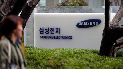 In this March 24, 2017 photo, a woman walks past a logo of Samsung Electronics in Seoul, South Korea. Samsung Electronics said Friday, April 7, 2017 its first-quarter profit jumped 48 percent likely due to smartphone component sales.