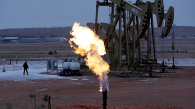 In this Oct. 22, 2015 file photo, workers tend to oil pump jacks behind a natural gas flare near Watford City, N.D.