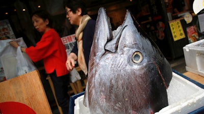Customers walk past the head of a bluefin tuna in front of a seafood restaurant at Tsukiji fish market in Tokyo Tuesday, May 16, 2017. Criminal and civil cases allege executives at the largest canned tuna companies were agreeing to collectively raise prices and limit promotions. Major retailers are taking aim at the most popular tuna brands in the U.S. - Chicken of the Sea, Bumble Bee and StarKist - saying they conspired to keep prices high for consumers.