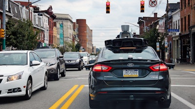 In this Wednesday, Sept. 14, 2016, file photo, a self-driving Uber car stops at a red light on Liberty Avenue through the Bloomfield neighborhood of Pittsburgh. In just a few years, well-mannered self-driving robotaxis will share the roads with reckless, law-breaking human drivers. The prospect is causing migraines for the people developing the robocars and is slowing their development. But experts say eventually the cars will coexist with human drivers on real roads.