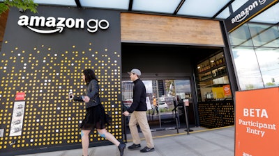 In this file photo, people walk past an Amazon Go store, currently open only to Amazon employees, in Seattle. Amazon Go shops are convenience stores that don't use cashiers or checkout lines, but a tracking system of sensors, algorithms, and cameras to determine what a customer has bought.