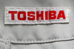 In this Thursday, June 15, 2017, photo, the logo of Toshiba Corp., Japan's electronics and energy company, is seen on a worker's jacket in Yokosuka, near Tokyo. Tokyo-based Toshiba, whose U.S. nuclear unit Westinghouse Electric Co. filed for bankruptcy protection in March, said Friday it received an extension until Aug. 10 to give its earnings report for the fiscal year that ended in March.