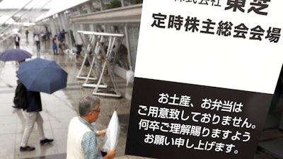 Toshiba shareholders arrive at the venue for the annual shareholders' meeting in Chiba, east of Tokyo, Wednesday, June 28, 2017. Japanese electronics and energy giant Toshiba has delayed its deadline for reaching an agreement on selling its lucrative computer memory chip business. The company said Wednesday negotiations were continuing on a 2 trillion yen ($18 billion) deal with a consortium led by a Japanese government-backed fund. Tokyo-based Toshiba had hoped to have an agreement in time for Wednesday's shareholders meeting. The sign reads: 'Toshiba Corporation. The venue for the annual shareholders' meeting. Please do understand that we do not provide you souvenirs or lunch boxes.'