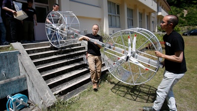 Members of Cartivator carry propellers of the test model flying car in Toyota, central Japan, Saturday, June 3, 2017. Cartivator Resource Management, in which Toyota invested 42.5 million yen ($386,000), showed reporters Saturday a test flight of a concoction of aluminum framing and propellers. It took off several times, hovering at eye level for a few seconds, before falling to the ground.