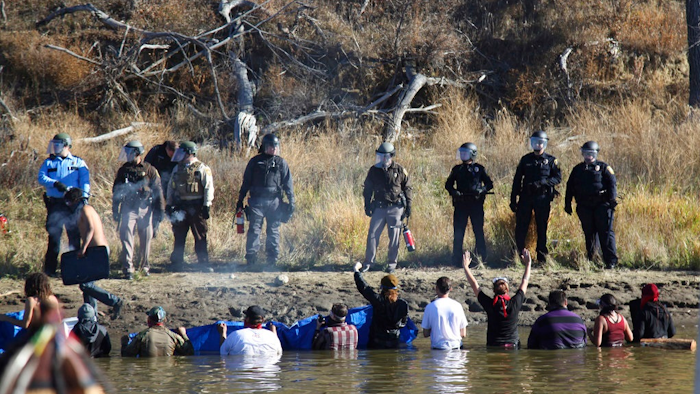 In this Nov. 2, 2016 file photo, protesters demonstrating against the expansion of the Dakota Access pipeline wade in cold creek waters confront local police near Cannon Ball, N.D. Industry officials say protests like the one involving the disputed pipeline may be commonplace in the future. The recently completed $3.8 billion pipeline that's opposed by American Indian tribes and others was discussed Wednesday, July 19, 2017, at an annual oil industry conference in Bismarck with a panel dissecting what was learned from the nearly year-long struggle over building it in North Dakota.