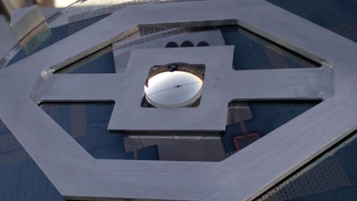 The concentrating photovoltaic system showing the top lenslet; the little black square visible near the middle is the solar cell and the lines running away from it are the contact wires.