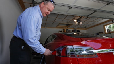 In this Thursday, July 13, 2017, photo, Jeff Solie plugs in his electric Tesla sedan at his home, in New Berlin, Wis. Electric cars are seeing growing support around the world. But there’s a problem: There aren’t enough places to plug those cars in. The nearest fast-charging Tesla Superchargers are 45 miles (72 kilometers) away. There are some public charging stations in nearby Milwaukee, at hotels and shopping centers, but Solie relies almost entirely on the charging system he set up in his garage.