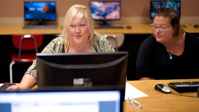 In this Thursday, July 27, 2017, photo, Cheryl Bast, left, is accompanied by her daughter Liz Pierson, as she works on an application for a position with Omaha Public Schools, during a job fair held at Omaha South High School in Omaha, Neb. On Friday, Aug. 4, 2017, the U.S. government issues the July jobs report.