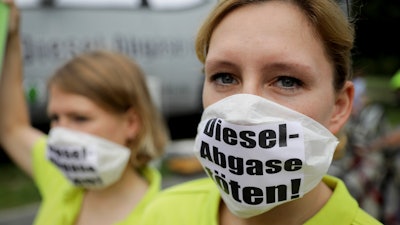 A demonstrator wearing a face mask with the inscription 'Kill diesel emissions' protests the 'Diesel Summit' that is to take place in Berlin, Germany, Wednesday, Aug. 2, 2017. German auto bosses, ministers and state governors are considering how to reduce diesel emissions as drivers face the threat of possible bans on driving older diesel cars in some cities. A meeting Wednesdayis to bring together leading politicians with bosses from Volkswagen, Porsche, Audi, Mercedes, BMW, Opel and Ford.