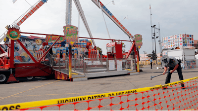 In this July 27, 2017 file photo, an Ohio State Highway Patrol trooper removes a ground spike in front of the fire ball ride at the Ohio State Fair in Columbus, Ohio. The Dutch manufacturer of a thrill ride that broke apart and killed an 18-year-old man at the Ohio State Fair says excessive corrosion on a support beam led to a “catastrophic failure.” A statement on KMG’s website dated Friday, Aug. 4, says the company officials visited the accident site and conducted metallurgical tests.