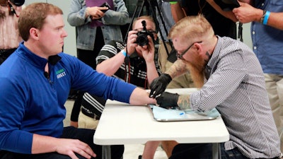 Tony Danna, left, vice president of international development at Three Square Market in River Falls, Wis., receives a microchip in his left hand at company headquarters Tuesday, Aug. 1, 2017. The company is making microchips available to its employees, allowing them to open doors, log onto their computers or buy breakroom snacks by simply waving their hand.