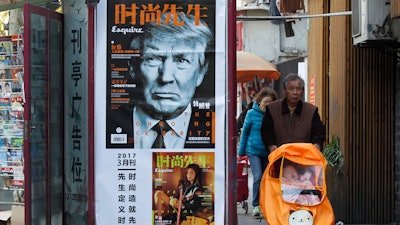 In this March 15, 2017 file photo, a man pushes a stroller past a magazine advertisement featuring U.S. President Donald Trump at a news stand in Shanghai, China. U.S. media reported Wednesday, Aug 2, 2017 that the administration of President Donald Trump is considering using rarely invoked U.S. trade laws to compel China to crack down on theft of copyrights, patents and other intellectual property and fend off technology sharing demands from Beijing.