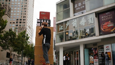 A deliver worker talks on his mobile phone next to a card loaded boxes of dried foods near a sushi restaurant at a commercial building in Beijing, Tuesday, Sept. 26, 2017. China has postponed enforcement of sweeping new controls on food imports following complaints by the United States, Europe and other trading partners that they would disrupt billions of dollars in trade.