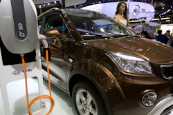 In this April 26, 2016, file photo, a staff member stands next to an e.Cool electric SUV by Chinese automaker Changjiang on display at the Beijing International Automotive Exhibition in Beijing. China has stepped up pressure on automakers to accelerate development of electric cars by raising the first-year target for a planned system of production quotas but delayed its rollout until 2019.