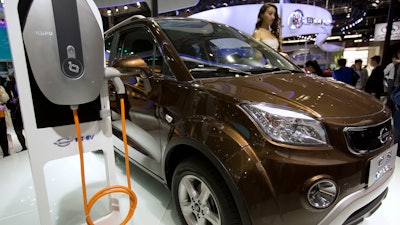 In this April 26, 2016, file photo, a staff member stands next to an e.Cool electric SUV by Chinese automaker Changjiang on display at the Beijing International Automotive Exhibition in Beijing. China has stepped up pressure on automakers to accelerate development of electric cars by raising the first-year target for a planned system of production quotas but delayed its rollout until 2019.