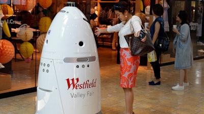 In this Monday, June 26, 2017, photo, Sophie Li, of Cupertino, Calif., offers to dance with a K5 robot made by Knightscope, Inc., at Westfield Valley Fair shopping center in San Jose, Calif. In the technology hotbed that stretches from San Francisco to San Jose, people can eat a pizza made largely by a robot, have hotel toiletries delivered by a robot, drink a frothy cappuccino made by a robot and shop at a mall with robot security. Now, one prominent San Francisco official is calling for a tax on companies that automate jobs once held by people.