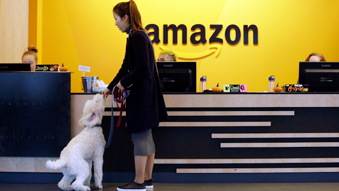 In this Wednesday, Oct. 11, 2017, photo, an Amazon employee gives her dog a biscuit as the pair head into a company building, where dogs are welcome, in Seattle. Whichever city lands Amazon’s second headquarters, some people in Seattle, it’s original hometown, say there are downsides to having the tech giant in the neighborhood.