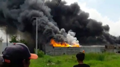 In this image made from video, residents watch as thick black smoke billows from the site of an explosion at a firecracker factory in Tangerang, on the outskirt of Jakarta, Indonesia, Thursday, Oct. 26, 2017. The explosion and raging fire killed a number of people and injured dozens, police said.
