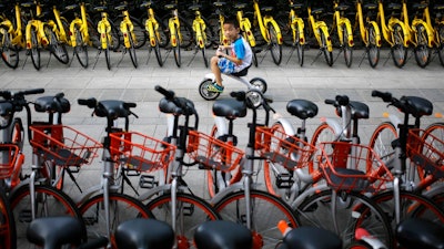 In this Aug. 31, 2017 file photo, a child rides past bicycles from bike-sharing companies parked along a sidewalk in Beijing. A report says China’s factory activity expanded in September at the fastest pace in five years, indicating a healthy outlook for the world’s second-biggest economy.