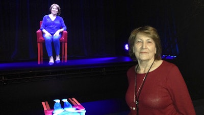 In this Oct. 20, 2017 photo, Holocaust survivor Fritzie Fritzshall poses for a portrait in front of her 3D hologram at the Illinois Holocaust Museum in Skokie, Ill. Fritzshall is one of 13 Holocaust survivors who tell their stories through holographic images that invite the audience to ask questions, creating what feels like a live conversation. The exhibit in Skokie marks the first time that the voice-recognition technology powering conversations with audiences has been married to 3-D holographic technology to tell survivors' stories.