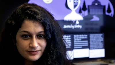 In this Tuesday, Oct. 24, 2017 photo, co-creator of a fiction-writing 'chatbot,' Massachusetts Institute of Technology postdoctoral associate Pinar Yanardag, of Istanbul, Turkey, sits for a photograph in front of a graphic from the home page of the site called 'Shelley.' Named after 'Frankenstein' author Mary Shelley, the chatbot has been trained on more than 140,000 horror stories written by amateur writers on a popular online forum. Now Shelley is generating its own stories on Twitter, taking turns with humans in an experiment to find out if artificial intelligence is smart enough to make someone feel scared.