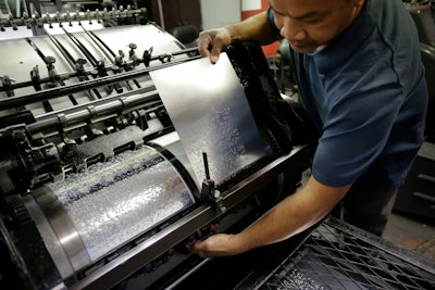 In this Tuesday, Oct. 17, 2017 photo press operator Cham Cha, of Cranston, R.I., attaches a braille plate to a printing press at the National Braille Press in Boston. The Boston-based organization has been a leading force for braille literacy in the U.S., since its founding as a weekly newspaper for the blind in 1927. But it is now confronting a record low literacy in the writing system for the blind as it marks its 90th birthday this year.