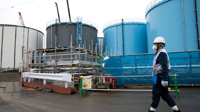In this Feb. 23, 2017, file photo, an employee walks past storage tanks for contaminated water at the tsunami-crippled Fukushima Dai-ichi nuclear power plant of the Tokyo Electric Power Co. (TEPCO) in Okuma town, Fukushima prefecture, Japan. More than six years after a tsunami overwhelmed the Fukushima nuclear power plant, Japan has yet to reach consensus on what to do with a million tons of radioactive water, stored on site in around 900 large and densely packed tanks that could spill should another major earthquake or tsunami strike.