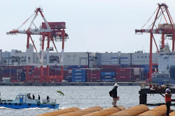 In this March 24, 2017, photo, workers stand at a seaside construction site with the pier of a container terminal in the background in Tokyo. Japan's trade surplus fell more than 40 percent in October from a year earlier, despite strong growth in exports to China, the U.S. and the EU, as costs for imports of oil, gas and coal surged. Customs figures released Monday, Nov. 20, 2017, showed imports rose almost 19 percent from the same month a year earlier in October to 6.41 trillion yen ($57 billion) while exports were up 14 percent at 6.7 trillion yen ($59 billion).