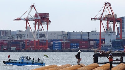 In this March 24, 2017, photo, workers stand at a seaside construction site with the pier of a container terminal in the background in Tokyo. Japan's trade surplus fell more than 40 percent in October from a year earlier, despite strong growth in exports to China, the U.S. and the EU, as costs for imports of oil, gas and coal surged. Customs figures released Monday, Nov. 20, 2017, showed imports rose almost 19 percent from the same month a year earlier in October to 6.41 trillion yen ($57 billion) while exports were up 14 percent at 6.7 trillion yen ($59 billion).