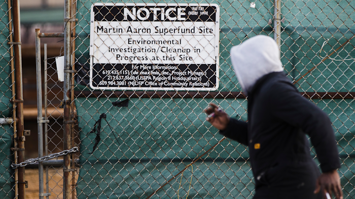 In this Dec. 11, 2017 photo, a man walks past a notice for the Martin Aaron Inc. Superfund site in Camden, N.J. Nearly 2 million people in the U.S. who live within a mile of 327 Superfund sites in areas prone to flooding or vulnerable to rising seas caused by climate change, according to an Associated Press analysis of flood zone maps, census data and U.S. Environmental Protection Agency records.