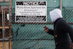 In this Dec. 11, 2017 photo, a man walks past a notice for the Martin Aaron Inc. Superfund site in Camden, N.J. Nearly 2 million people in the U.S. who live within a mile of 327 Superfund sites in areas prone to flooding or vulnerable to rising seas caused by climate change, according to an Associated Press analysis of flood zone maps, census data and U.S. Environmental Protection Agency records.