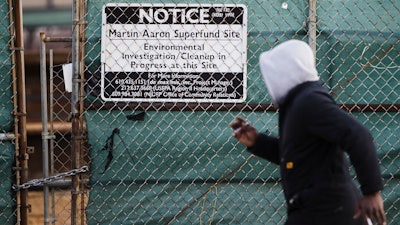 In this Dec. 11, 2017 photo, a man walks past a notice for the Martin Aaron Inc. Superfund site in Camden, N.J. Nearly 2 million people in the U.S. who live within a mile of 327 Superfund sites in areas prone to flooding or vulnerable to rising seas caused by climate change, according to an Associated Press analysis of flood zone maps, census data and U.S. Environmental Protection Agency records.
