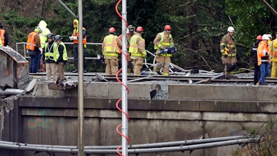 Workers stand atop a damaged railroad bridge at the scene of an Amtrak train crash onto Interstate 5 a day earlier Tuesday, Dec. 19, 2017, in DuPont, Wash. Federal investigators say they don't yet know why the Amtrak train was traveling 50 mph over the speed limit when it derailed Monday south of Seattle.