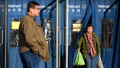 A shopper carries grocery bags as she exits a Walmart store in Beijing, Wednesday, Dec. 6, 2017. U.S. companies in China are seeing their sales improve but are frustrated by policies and regulatory barriers that block better access to the country's lucrative market, according to a survey released Wednesday.