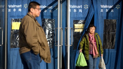 A shopper carries grocery bags as she exits a Walmart store in Beijing, Wednesday, Dec. 6, 2017. U.S. companies in China are seeing their sales improve but are frustrated by policies and regulatory barriers that block better access to the country's lucrative market, according to a survey released Wednesday.